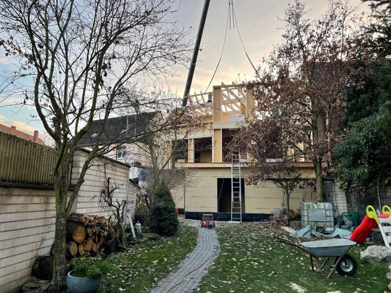 Ein Kran hebt in einem Hinterhof eine Holzkonstruktion an.