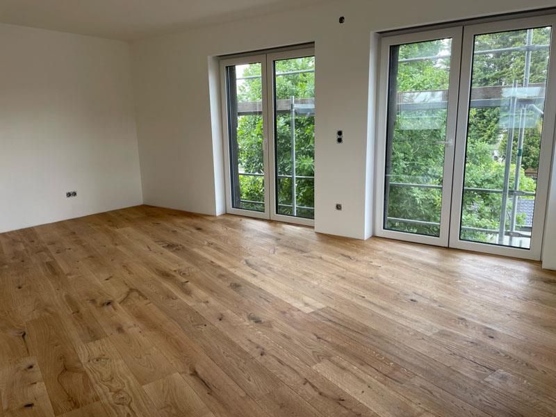 Ein leerer Raum mit Hartholzböden und vielen Fenstern.