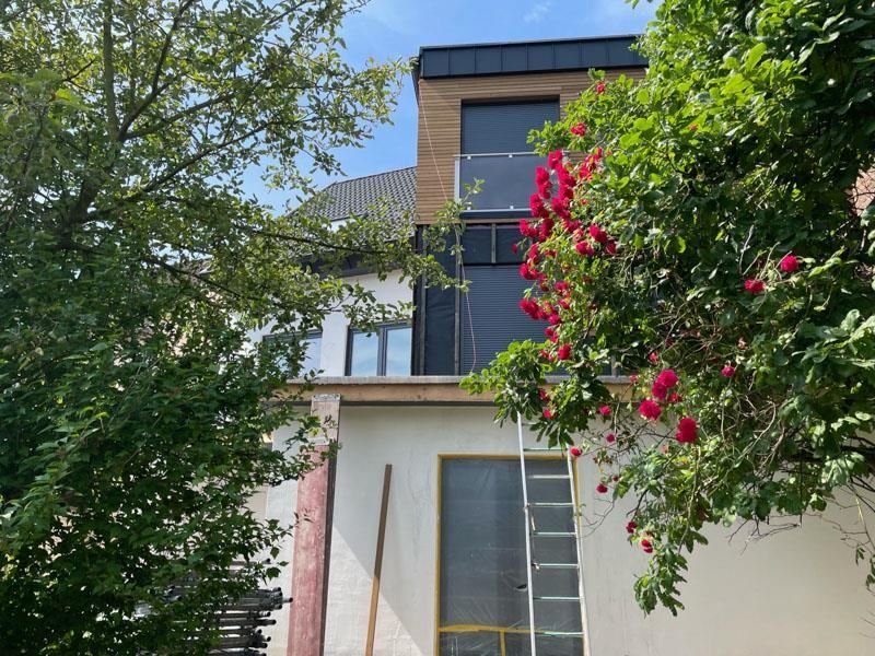 Ein Haus mit einer Leiter davor und einem Baum mit roten Blumen.