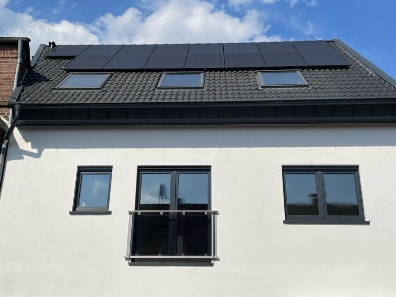 Ein weißes Haus mit schwarzen Fenstern und Solarzellen auf dem Dach.