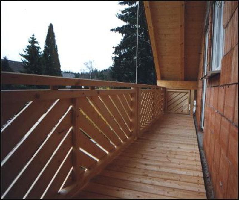 Ein Balkon mit Holzgeländer und Bäumen im Hintergrund