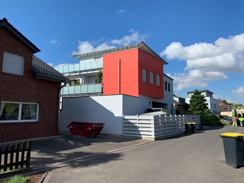 Ein roter Müllcontainer steht vor einem Haus