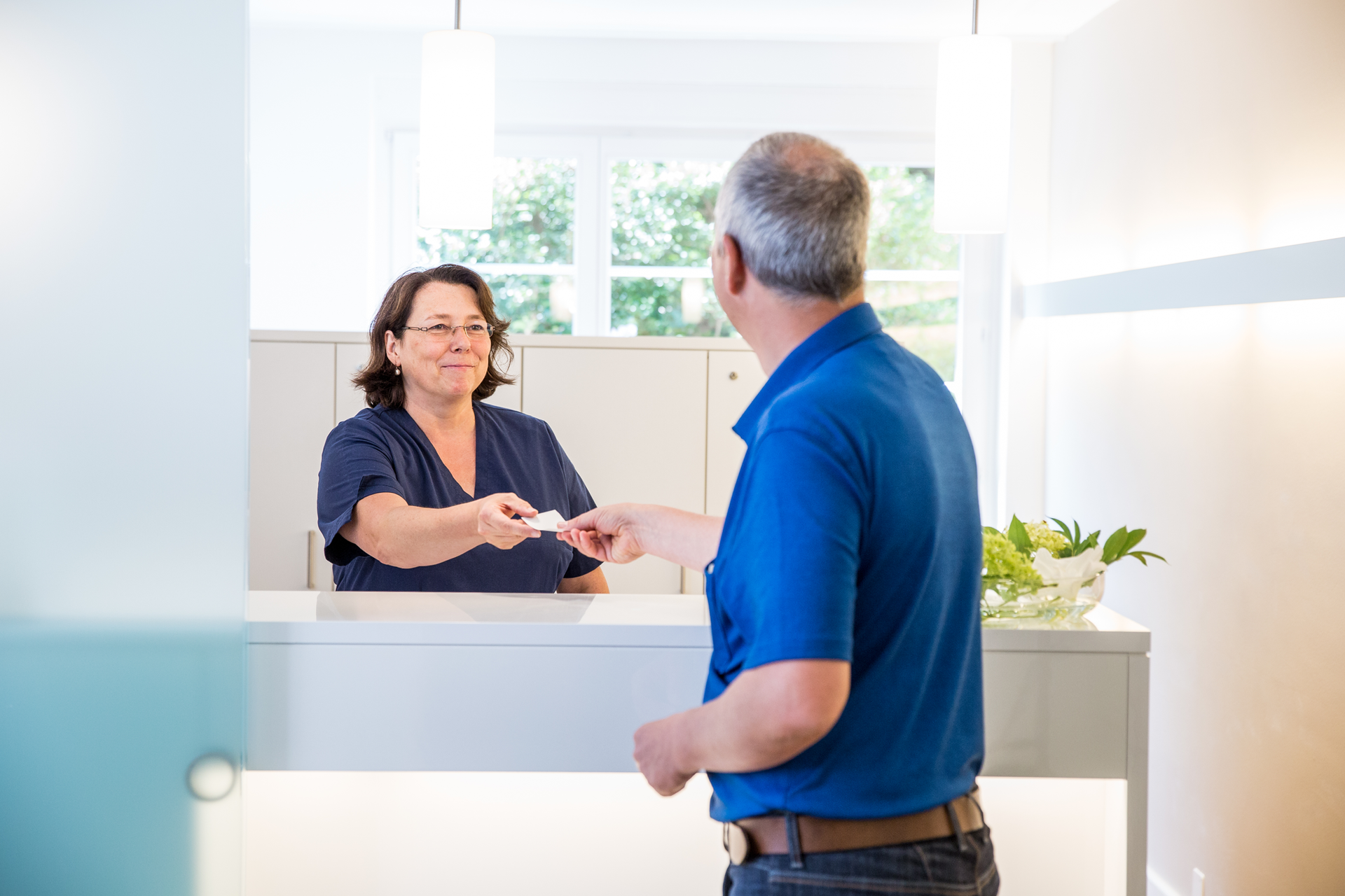 Ein Mann gibt einer Frau in einer Zahnarztpraxis eine Kreditkarte.