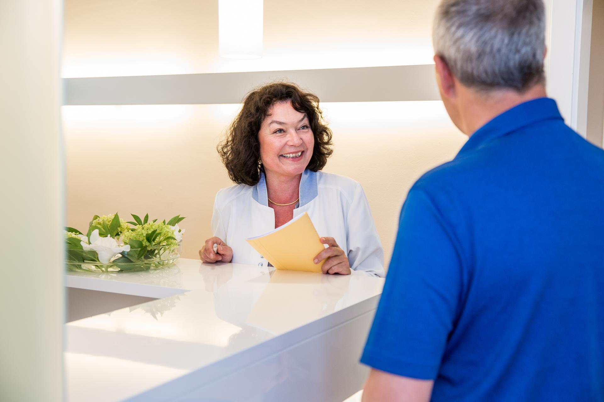 Eine Frau spricht mit einem Mann am Tresen einer Zahnarztpraxis.