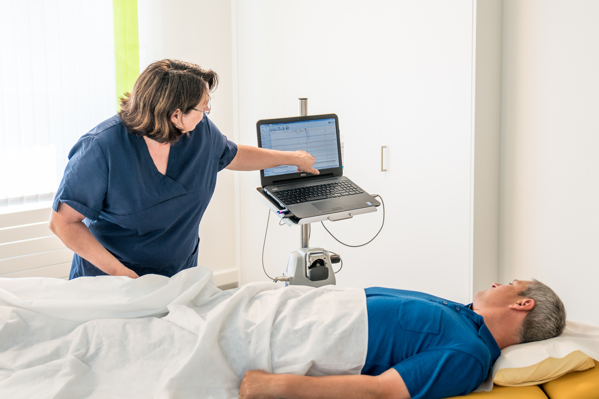 Eine Frau steht neben einem Mann, der in einem Krankenhausbett liegt.