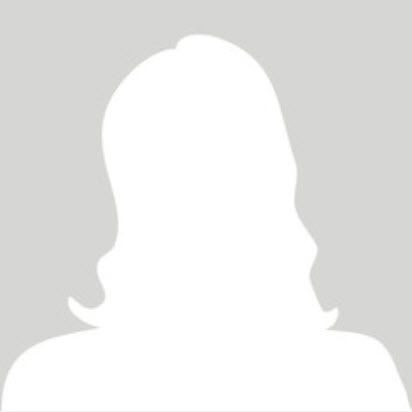 Eine Frau in einem weißen Kittel und einem blauen Hemd steht vor einem Fenster.