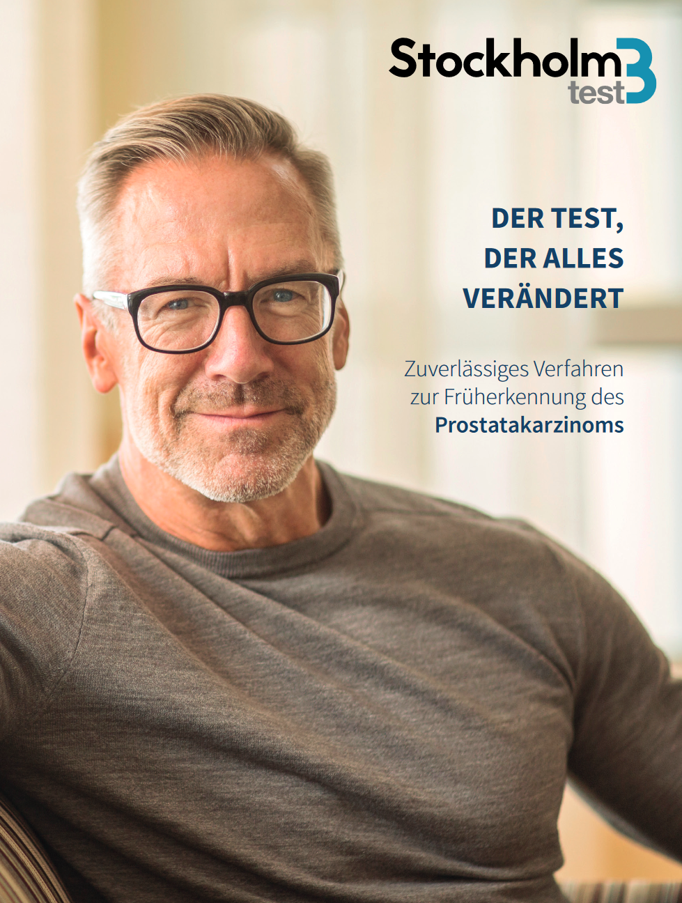 Ein Mann mit Brille sitzt auf einer Couch und lächelt.