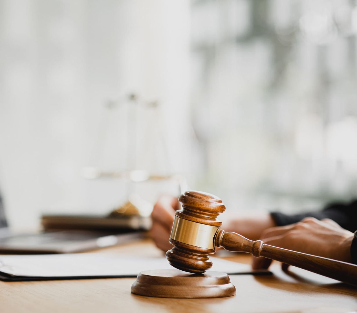 Persona que sostiene un mazo y lo golpea contra un bloque de madera; balanza de la justicia en el fondo.