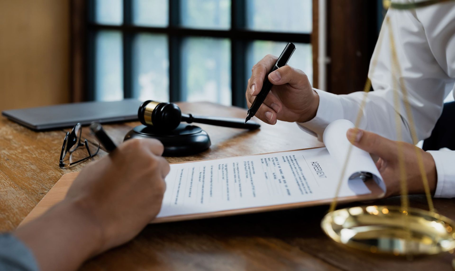 Dos personas firmando un documento en un escritorio, con un mazo y una balanza de la justicia presentes.
