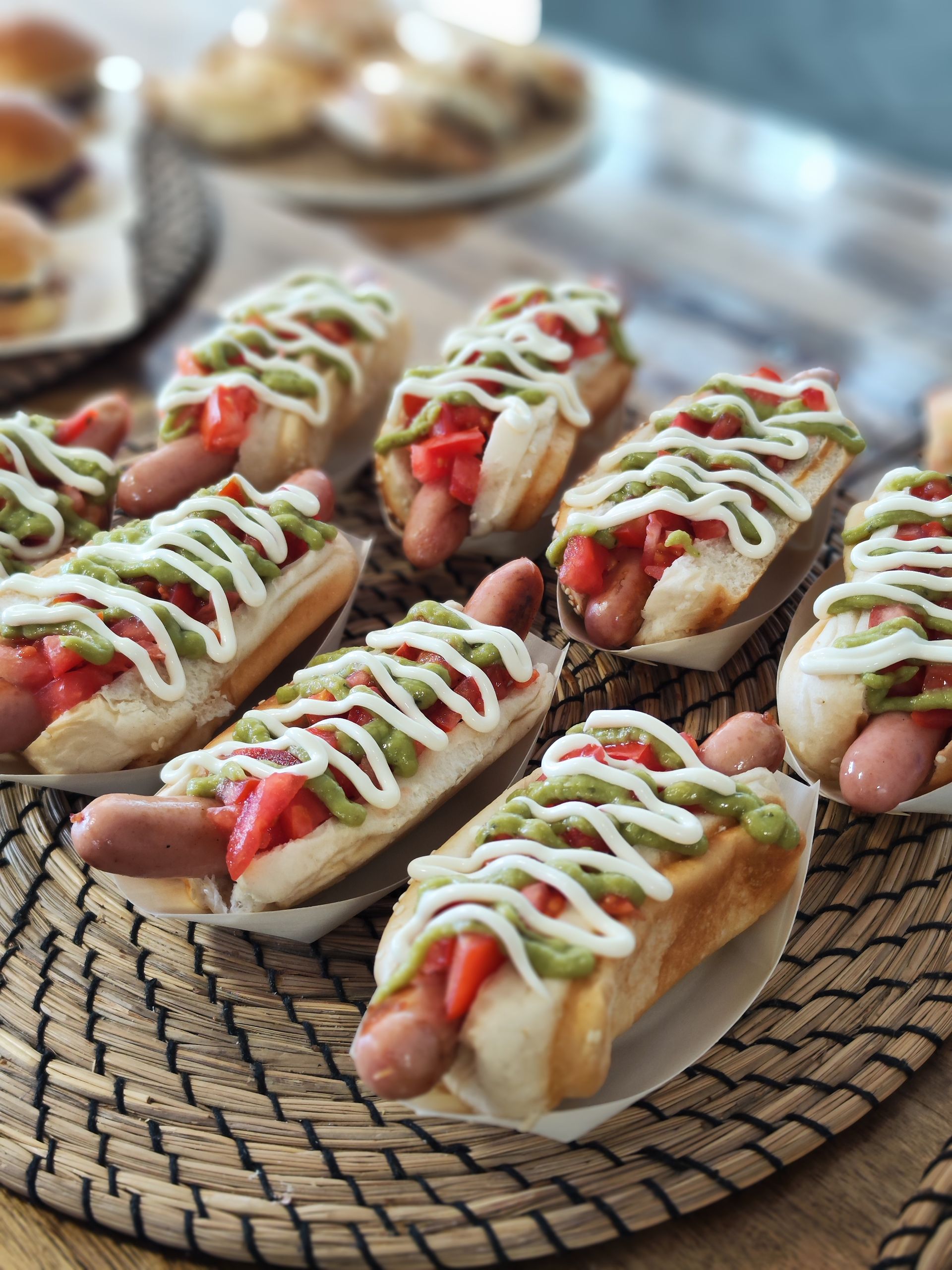 Un montón de perritos calientes con condimentos sobre una mesa.