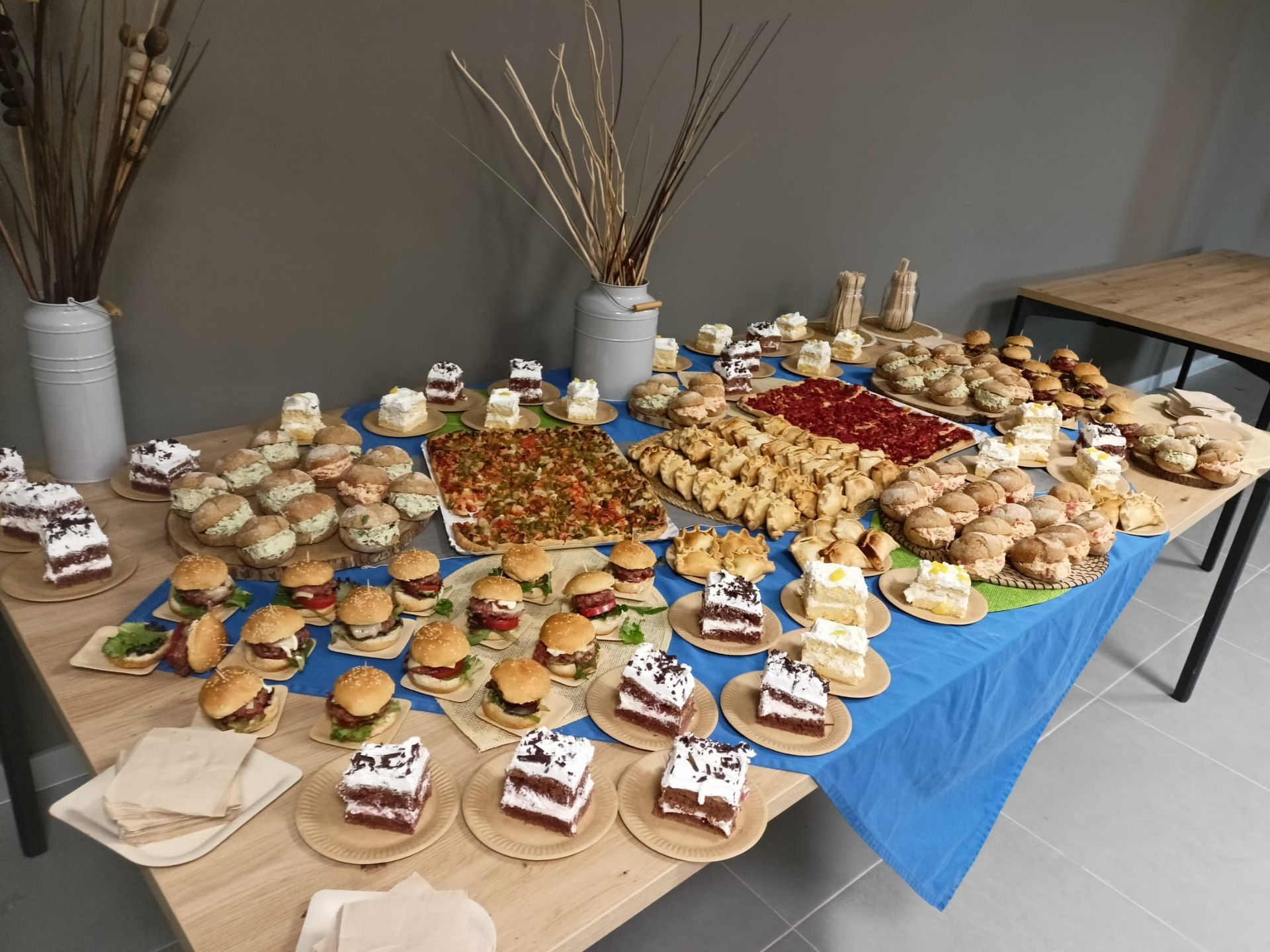 Una mesa llena de comida, incluyendo hamburguesas y pasteles.