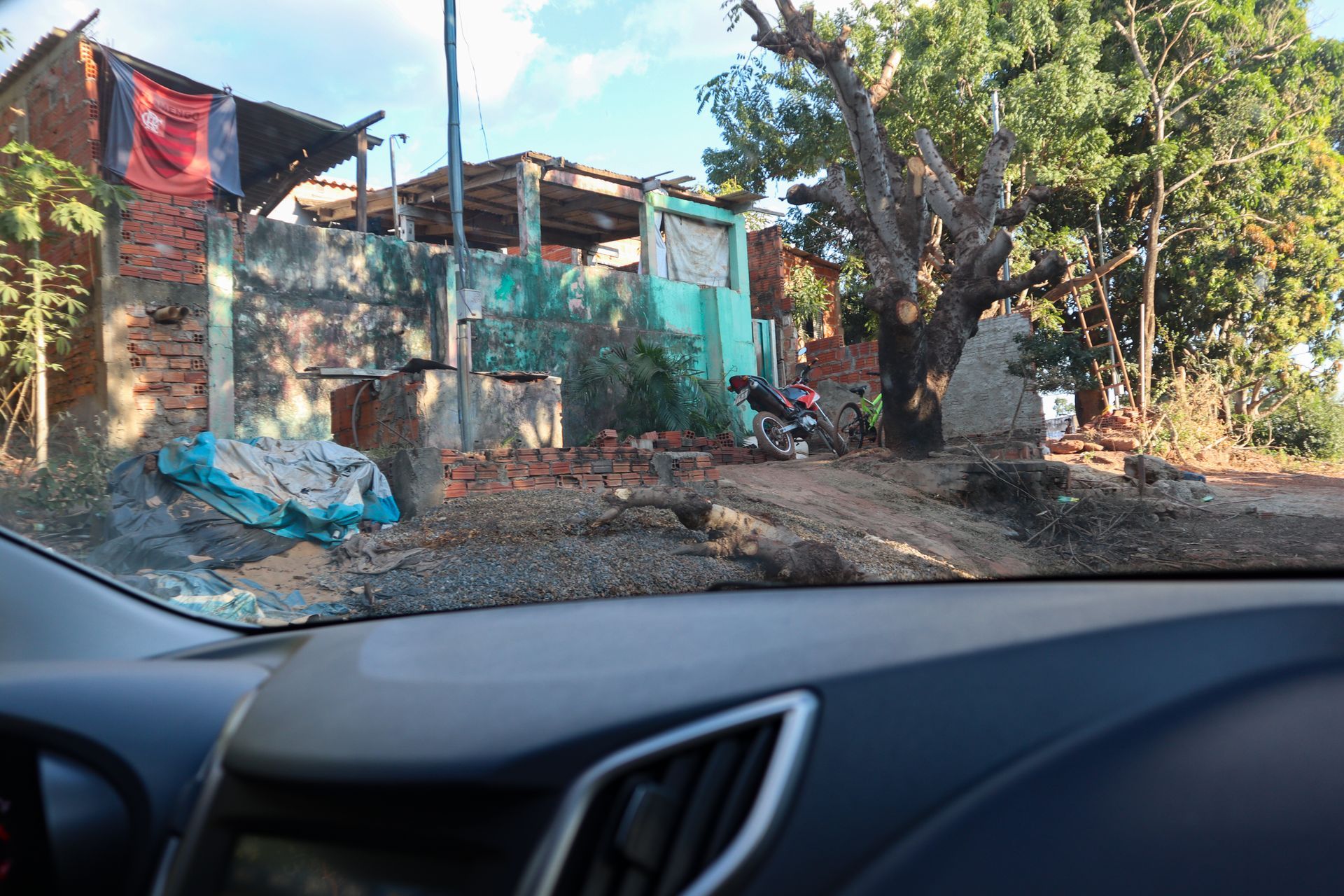 Blick aus dem Auto auf ein bescheidenes Haus mit türkisfarbenem Zaun, Bäumen und trockenem Laub im Garten