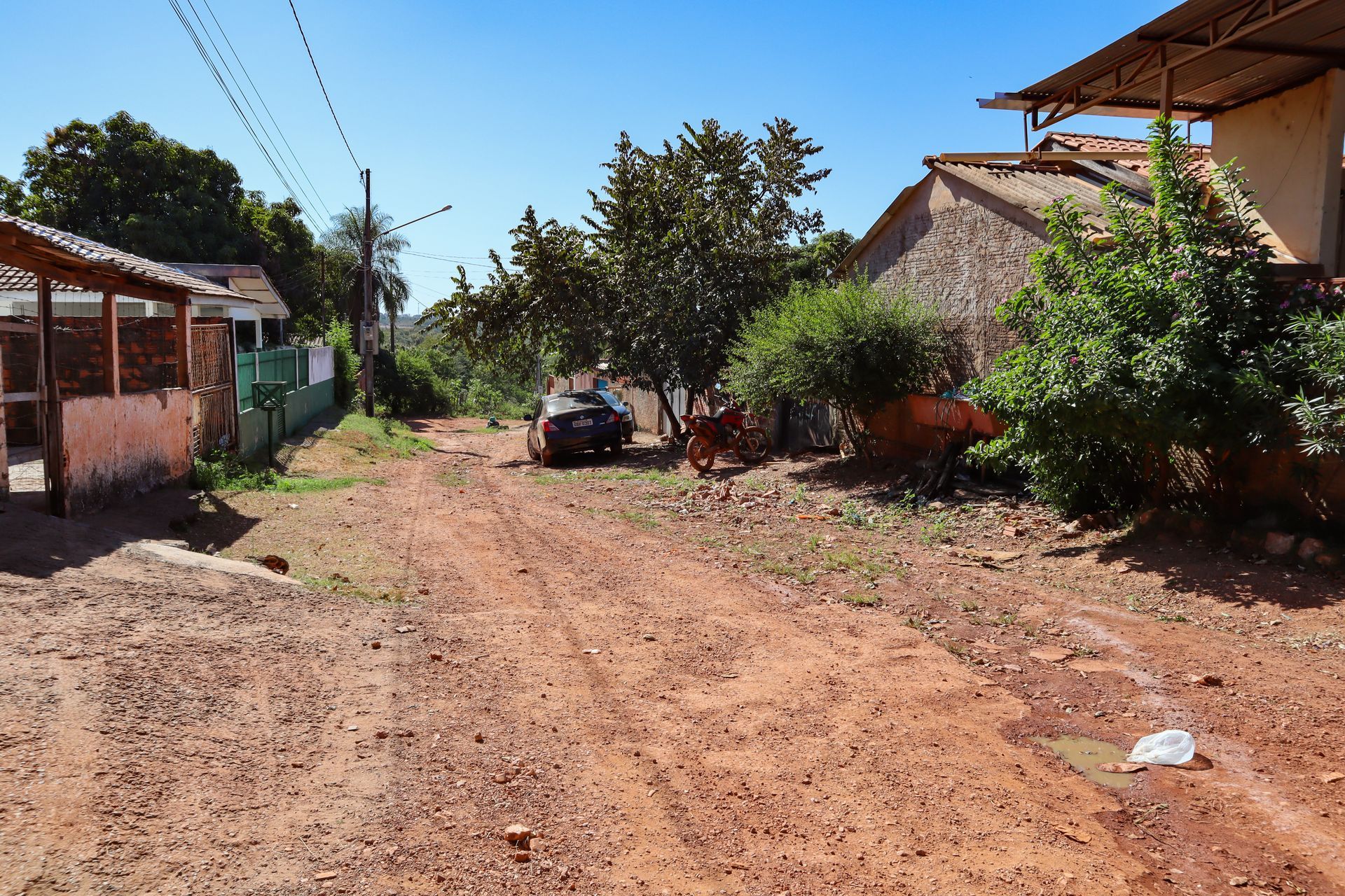 Feldweg in einer ländlichen Gegend mit Häusern, Bäumen und einem geparkten Fahrzeug unter blauem Himmel