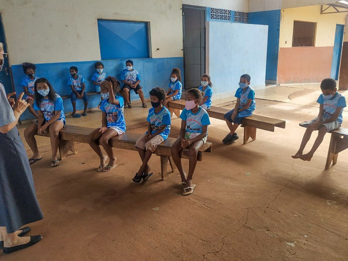 Schüler in blauen Uniformen sitzen auf Bänken in einem Klassenzimmer mit blauen Wänden und offenen Türen.