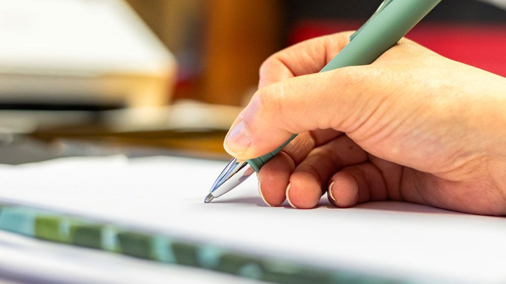 Eine Person schreibt mit einem Stift auf ein Blatt Papier.