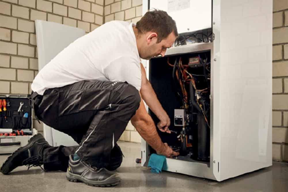 Ein Mann kniet vor einem Kühlschrank und repariert ihn .