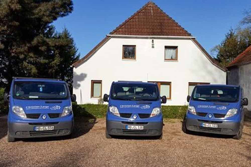 drei blaue Lieferwagen stehen vor einem weißen Haus