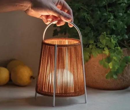 Mano sosteniendo una linterna encendida y tejida con un marco de metal blanco, junto a limones y follaje.