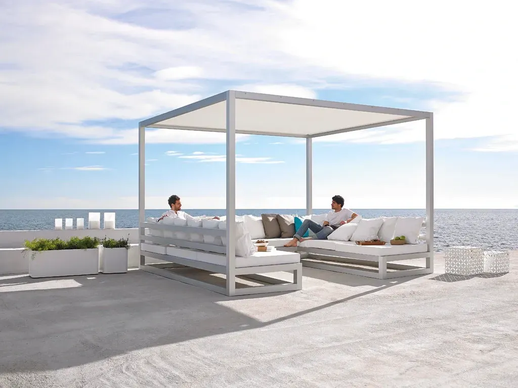 Dos personas se relajan en muebles de exterior blancos bajo un dosel junto al océano.