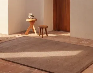 Habitación con alfombra marrón, pequeños taburetes de madera y luz solar proyectando una sombra.