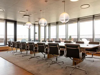 Sala de conferencias con mesa larga, sillas negras y amplios ventanales. Lámparas colgantes esféricas cuelgan del techo.