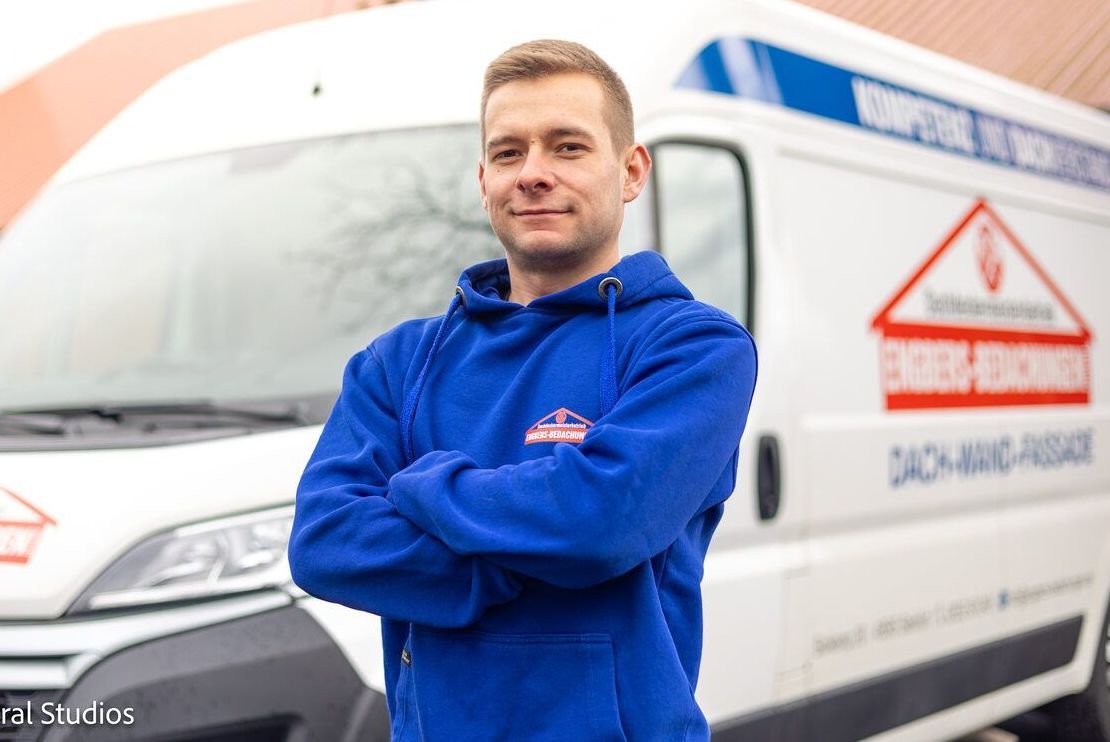 Ein Mann in einem blauen Sweatshirt steht vor einem weißen Lieferwagen.