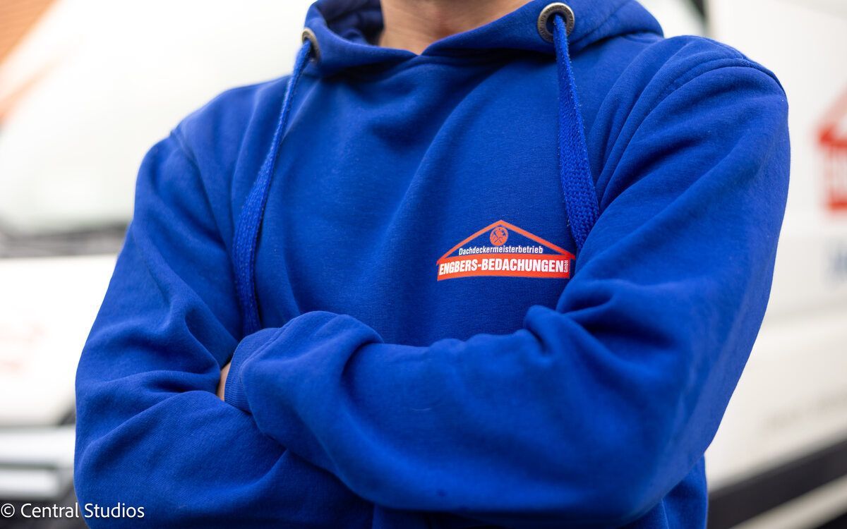 Ein Mann mit einem blauen Kapuzenpullover hat die Arme verschränkt
