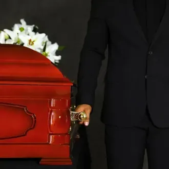 Un hombre con traje está de pie junto a un ataúd rojo.