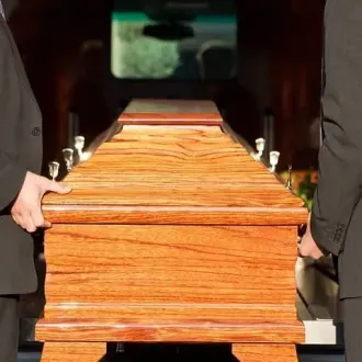 Dos hombres de traje sostienen un ataúd de madera.