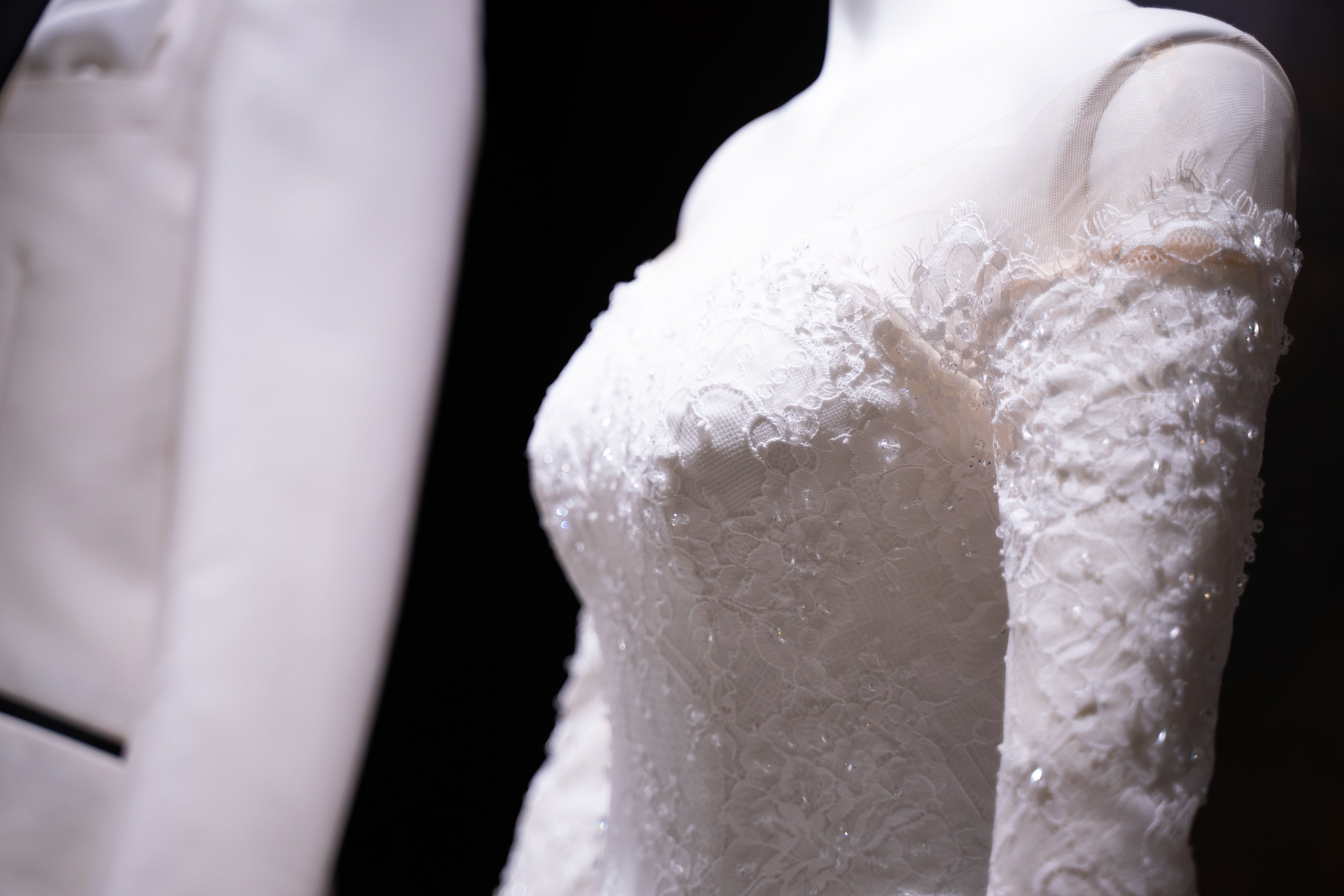 Un vestido de novia blanco está sobre un maniquí al lado de un esmoquin blanco.