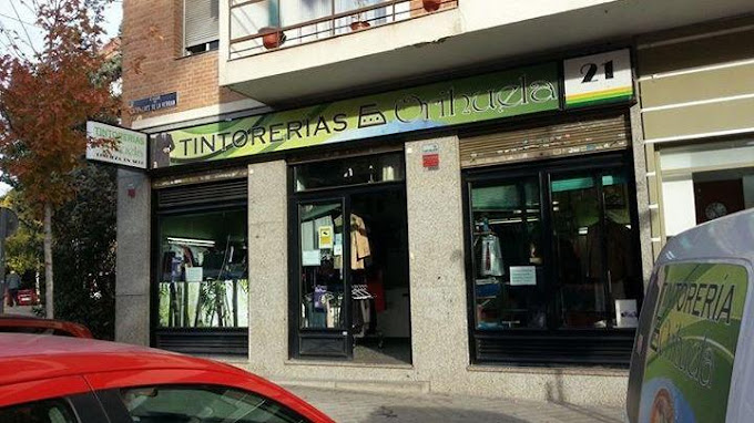 Un coche rojo está aparcado delante de una tienda llamada tintoreras