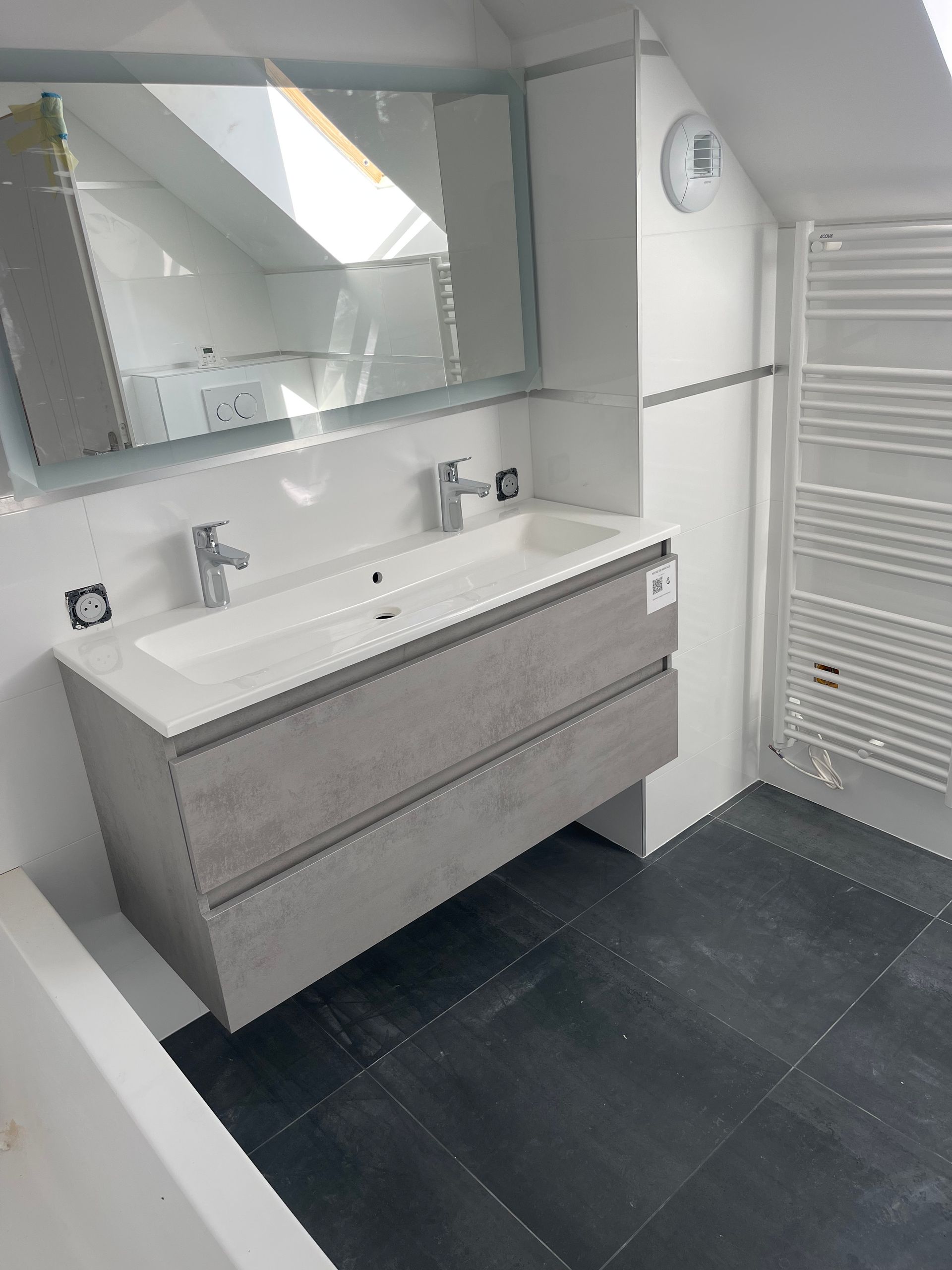 Meuble vasque gris, miroir et sèche-serviettes dans une salle de bains