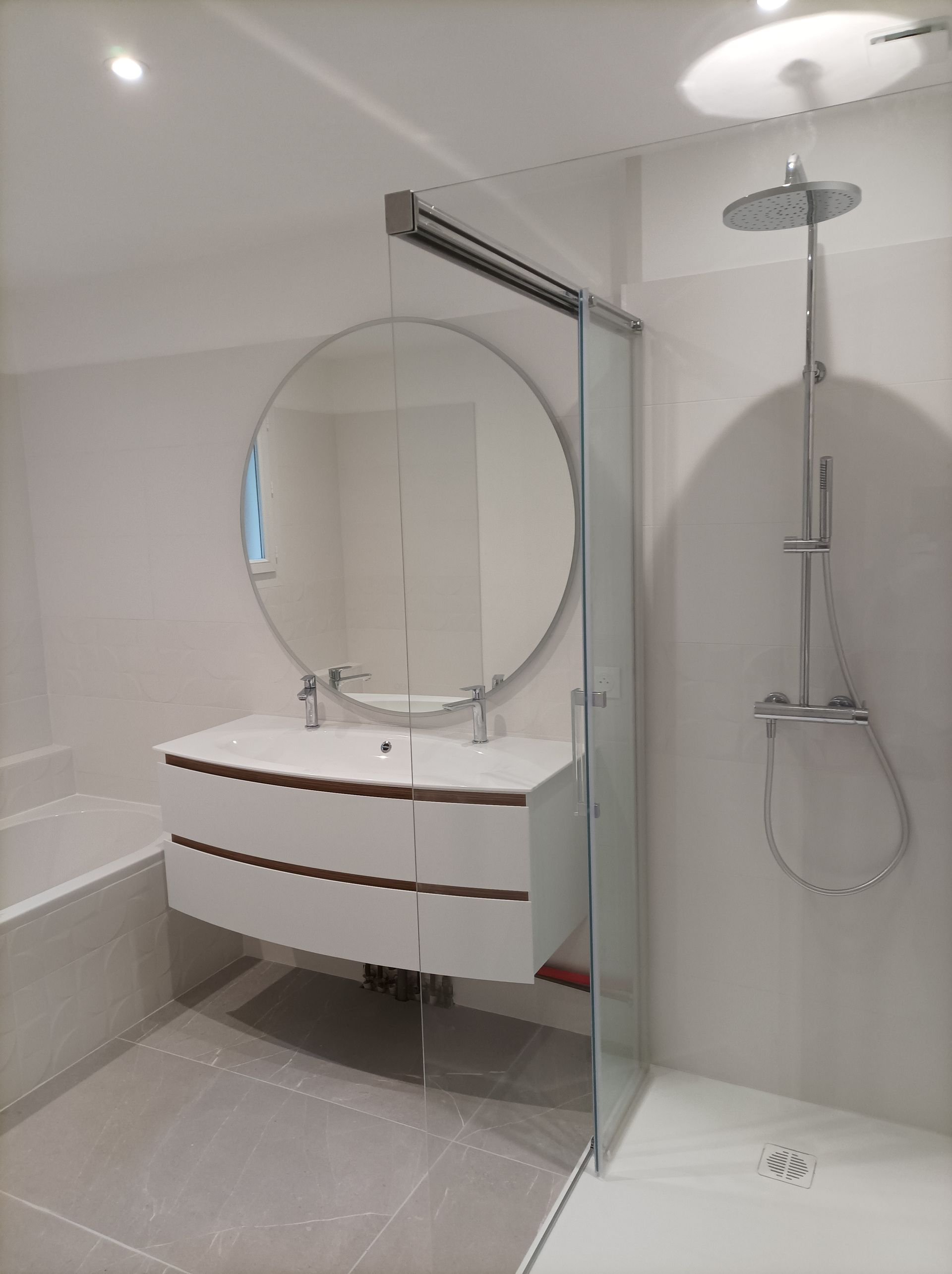 Un miroir rond accroché au-dessus d'un grand lavabo, le tout à côté d'une baignoire