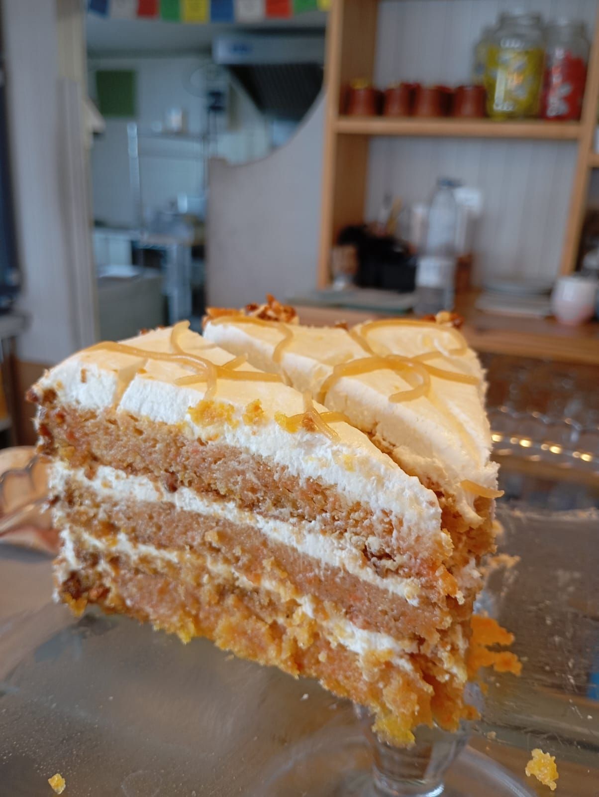 Una rebanada de pastel de zanahoria reposa sobre un plato de vidrio sobre una mesa.