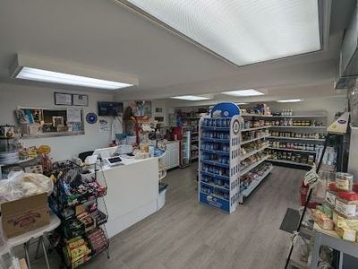 Innenansicht eines kleinen Lebensmittelladens mit weissem Bedientresen, Produktregalen und heller Deckenbeleuchtung.