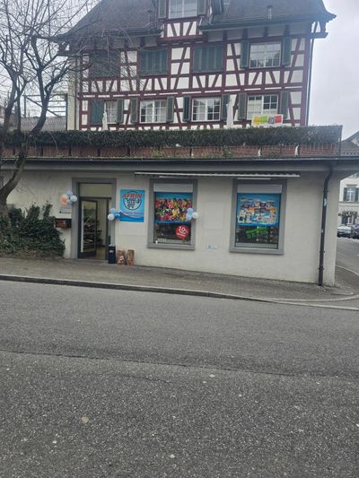 Ein historisches Fachwerkgebäude mit einem Ladenlokal im Erdgeschoss, das mit Auslagen, Plakaten und Luftballons geschmückt ist.
