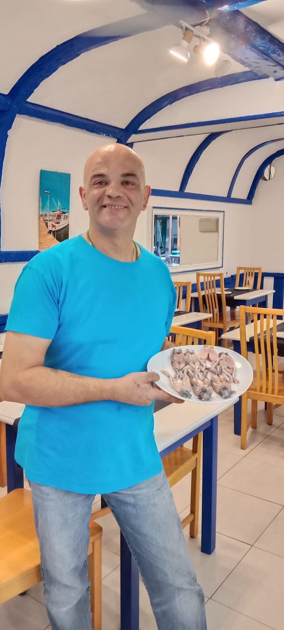 Hombre sosteniendo un plato de comida dentro de un restaurante con decoración azul y blanca.