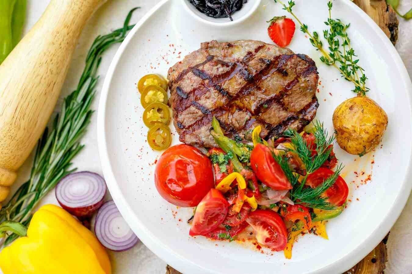 Bistec a la parrilla con ensalada en un plato blanco, servido en una mesa de madera.