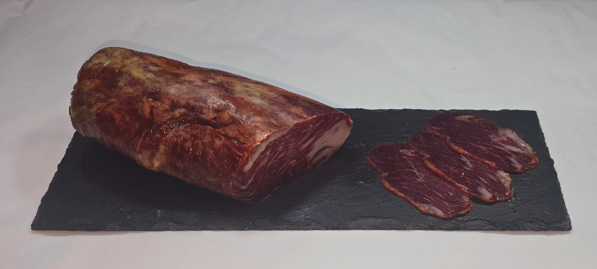 Un trozo de carne reposa sobre una tabla de cortar negra.