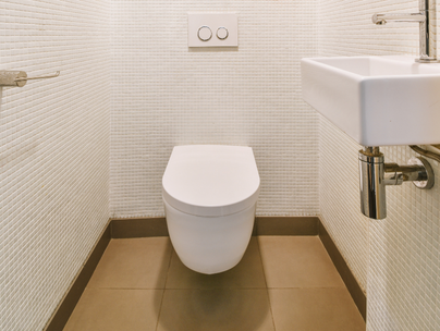 Toilettes et lavabo blancs dans une petite salle de bain avec des murs blancs texturés et un sol marron.