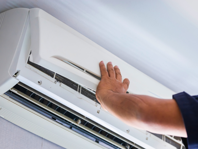 La main d'une personne touchant un climatiseur, un appareil blanc monté sur un mur blanc.