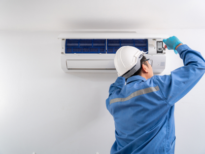 Technicien en CVC en uniforme bleu et casque de sécurité effectuant l'entretien d'un climatiseur mural.