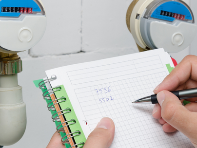 Une personne relève les compteurs d'eau et écrit les chiffres sur un bloc-notes à proximité de deux compteurs.