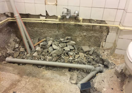 Rénovation de salle de bain : tas de gravats, tuyaux apparents et appareils de plomberie.