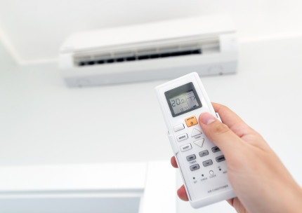 Main tenant une télécommande de climatiseur blanche, pointée vers une unité de climatisation murale réglée à 20 degrés.
