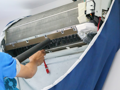 Personne nettoyant un climatiseur split avec un tuyau ; un couvercle bleu entoure l'appareil.