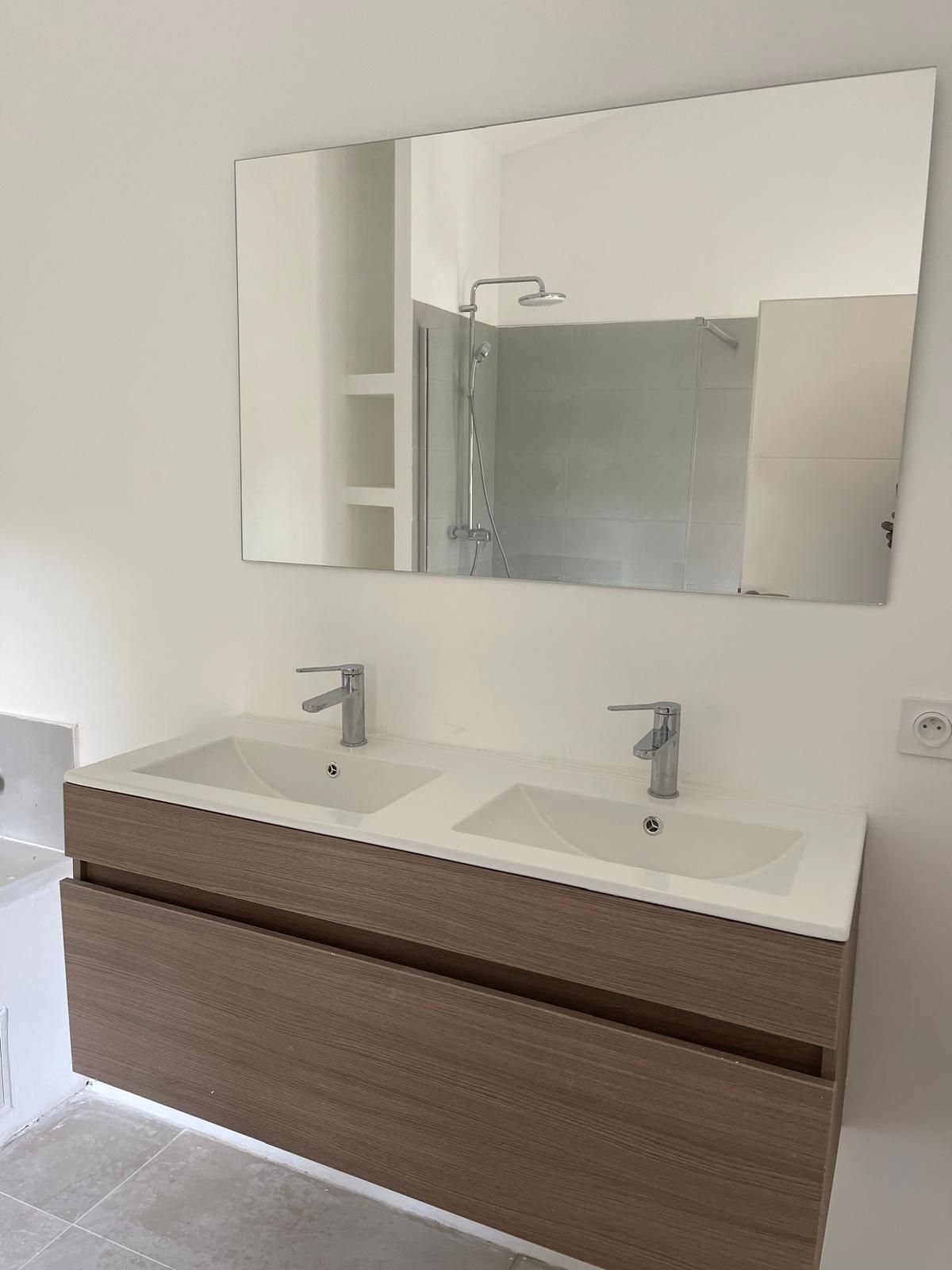 Meuble-lavabo avec deux vasques, un grand miroir et un meuble en bois. Murs blancs.