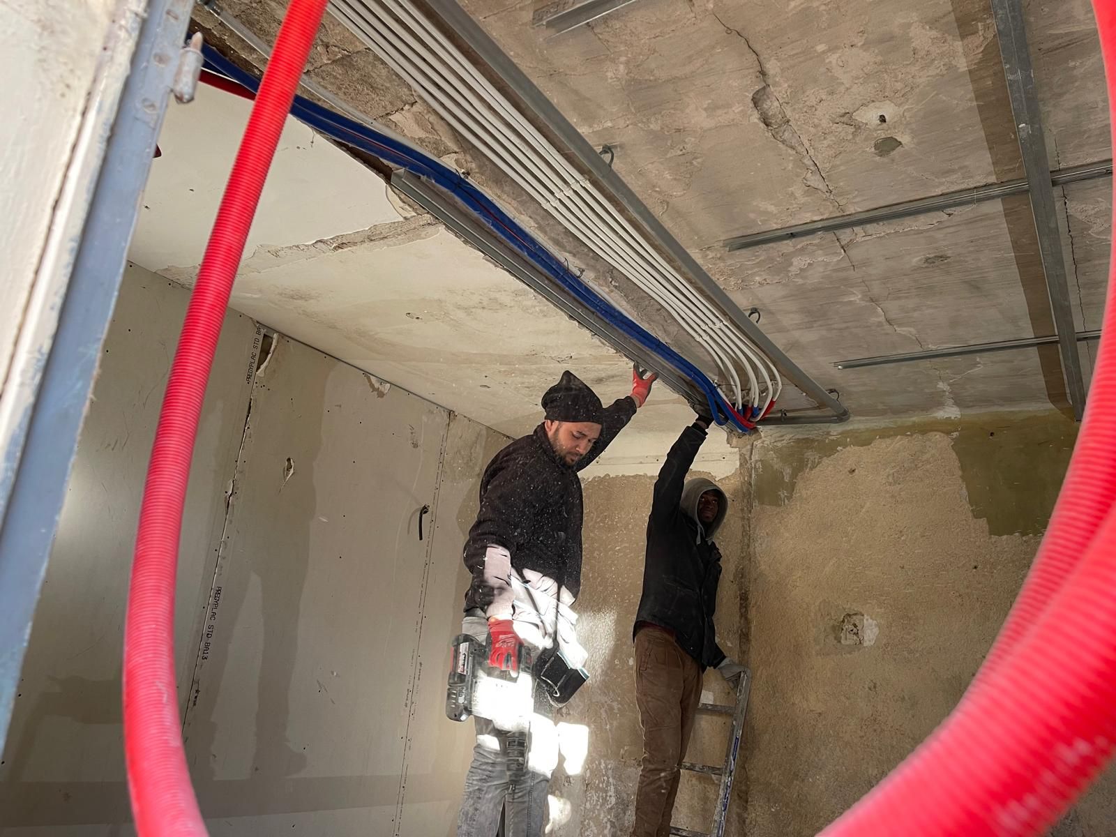 Deux ouvriers installent des conduits et du câblage électriques dans un bâtiment en construction.
