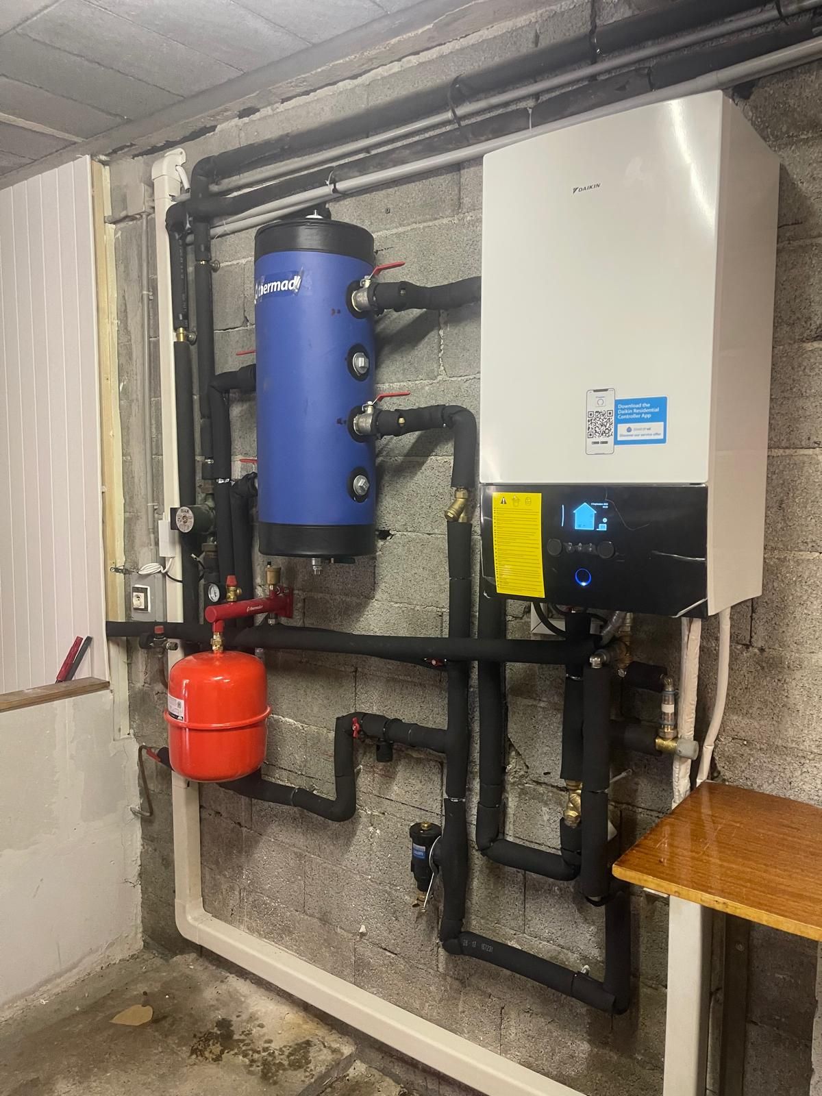 Système de chauffage : chaudière, chauffe-eau, vase d'expansion, tuyauterie montée sur un mur en béton.