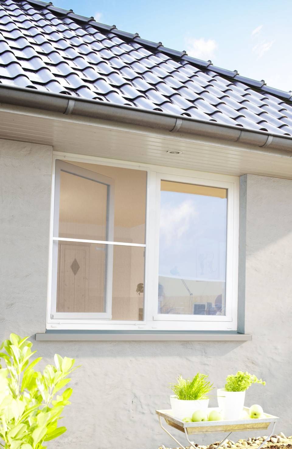 Weiß gerahmtes Fenster in einer hellen Wand mit schwarzem Ziegeldach.